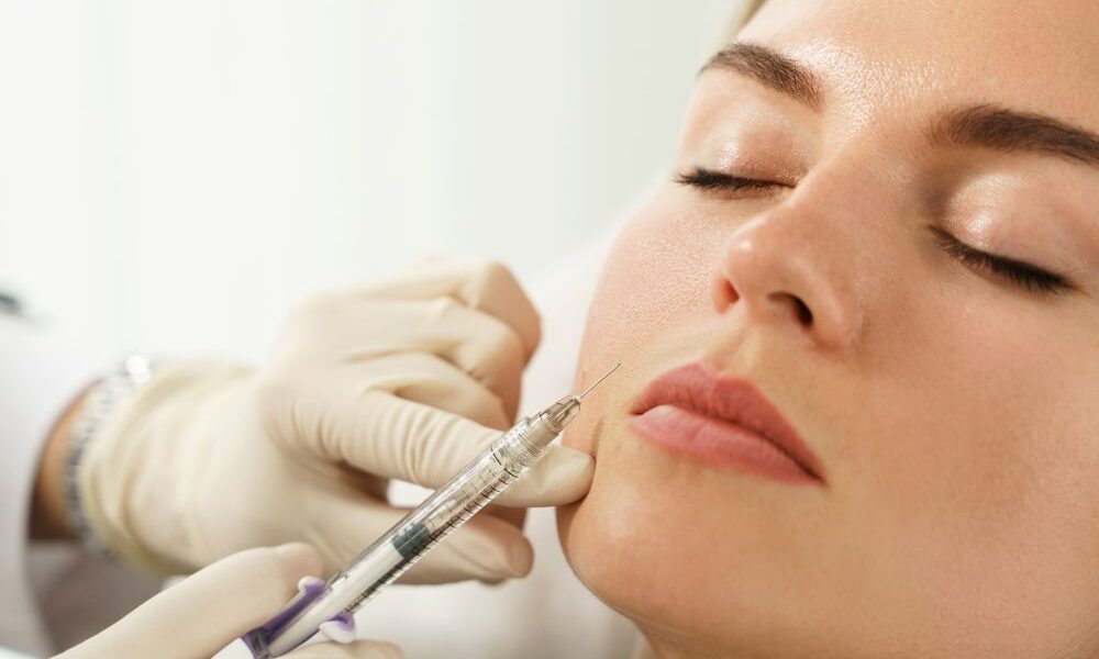 Profissional aplica injeção estética na face de paciente, em close, durante procedimento de harmonização facial com preenchimento dérmico.