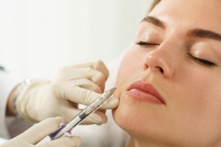 Profissional aplica injeção estética na face de paciente, em close, durante procedimento de harmonização facial com preenchimento dérmico.